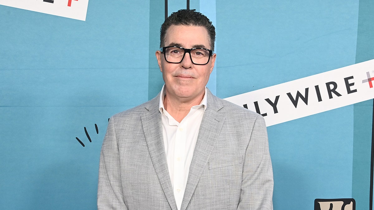 Adam Carolla wearing glasses and a suit on the red carpet