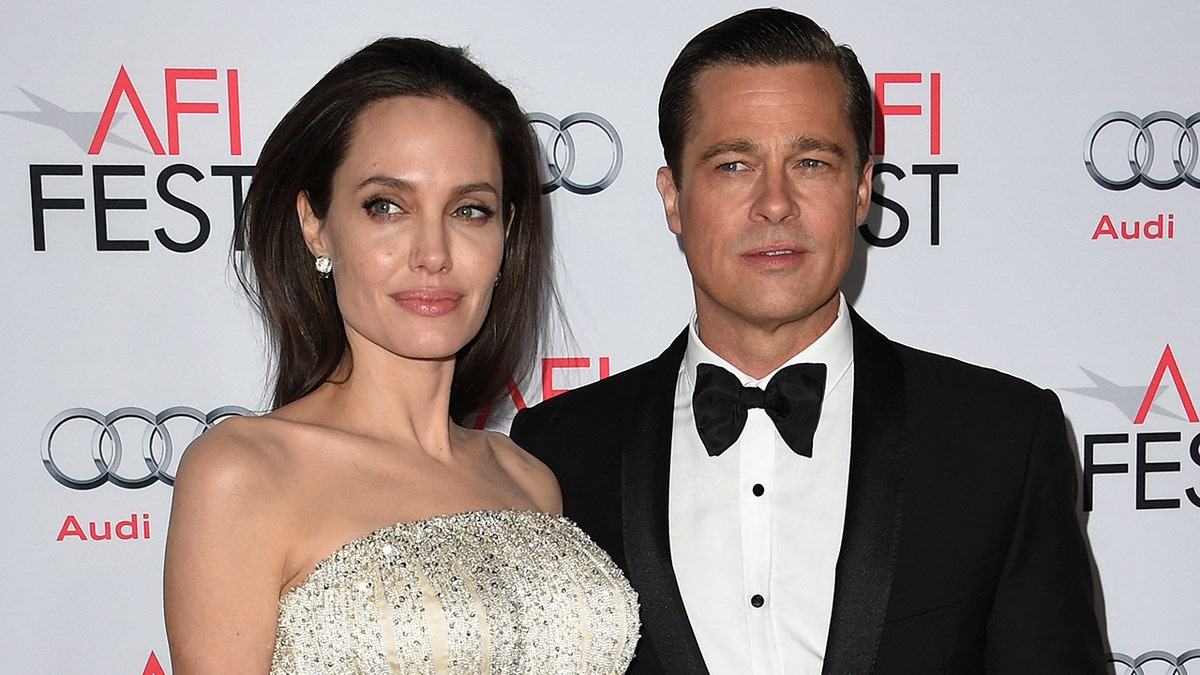 Angelina Jolie in a white and cream beaded strapless dress looks to her right with Brad Pitt, wearing a classic tuxedo also looking to his right