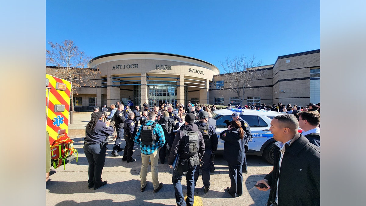 A crowd of civilians and police gathers in front of Antioch High School.