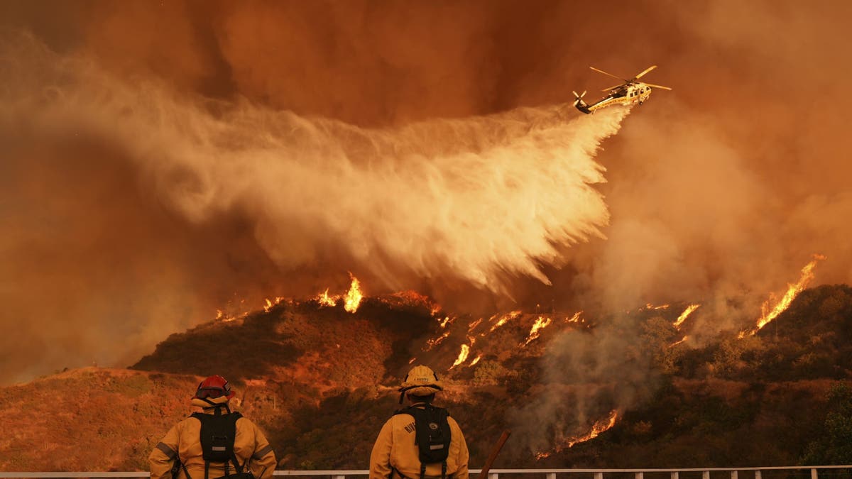 Firefighters watch as a helicopter drops water on the Palisades Fire in Mandeville Canyon in Los Angeles on January 11, 2025.