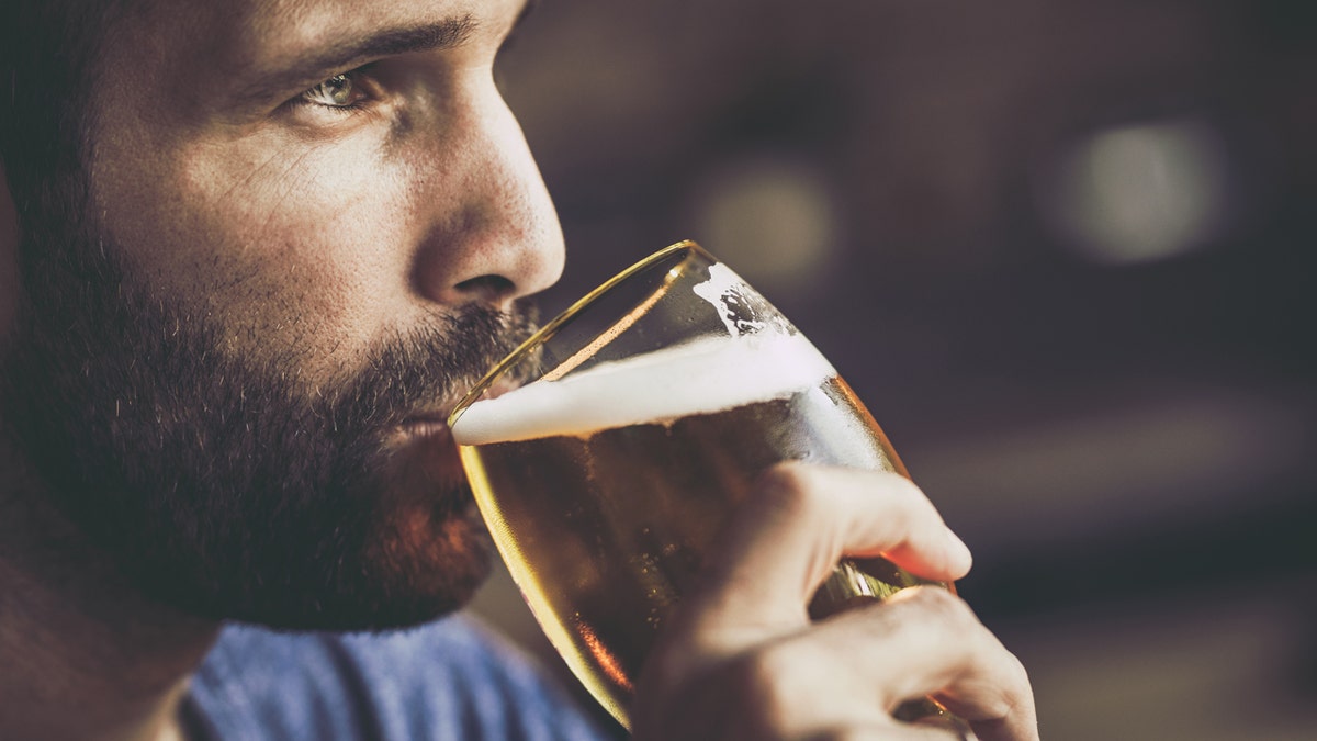 A bearded man is seen looking in front of him while drinking a beer.