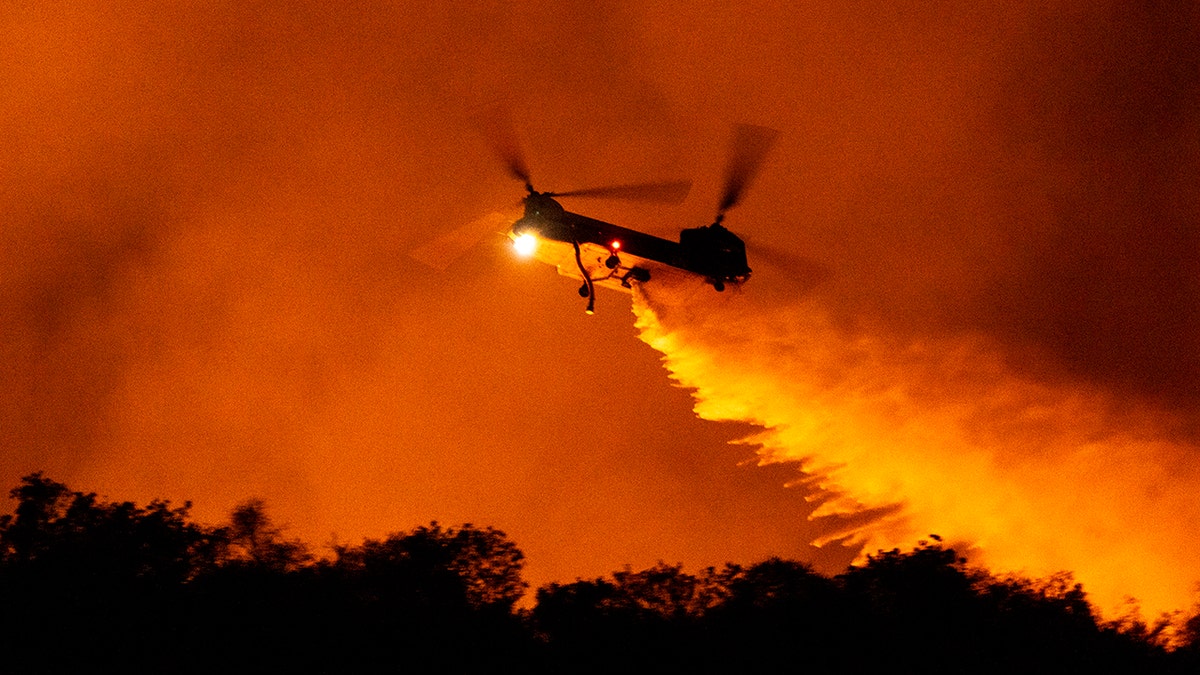 A helicopter drops water on the Palisades Fire