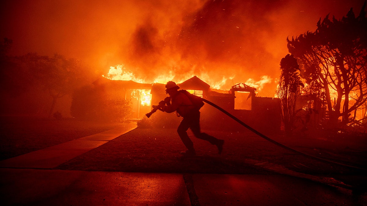 Firefighter with hose, house on fire behind him