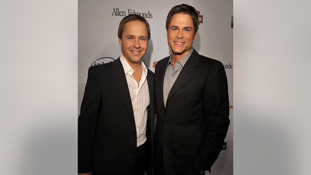 Chad Lowe with a black suit and the white button down smiles next to his older brother Rob Lowe with a black suit and gray shirt