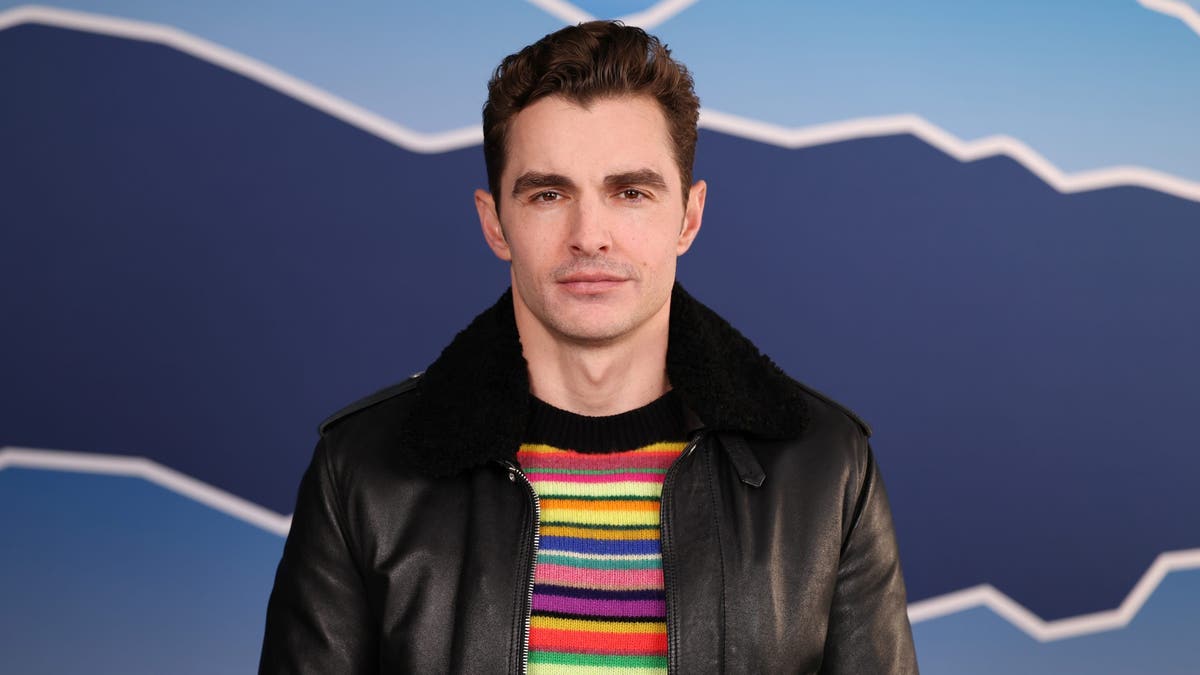 Dave Franco in a rainbow striped sweater and black leather jacket with a fur trim at Sundance