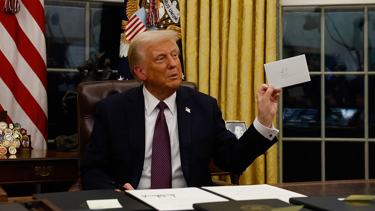 Donald Trump in the Oval Office holds a note from Joe Biden