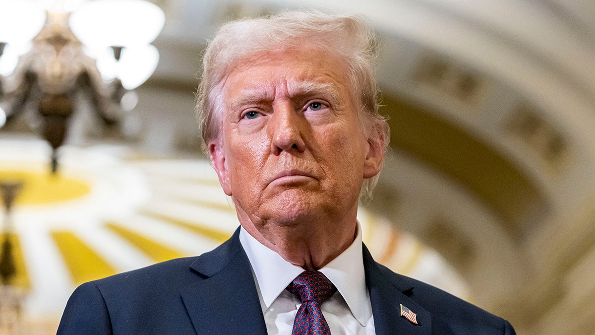 Donald Trump wearing a navy jacket and purple tie looks to his right