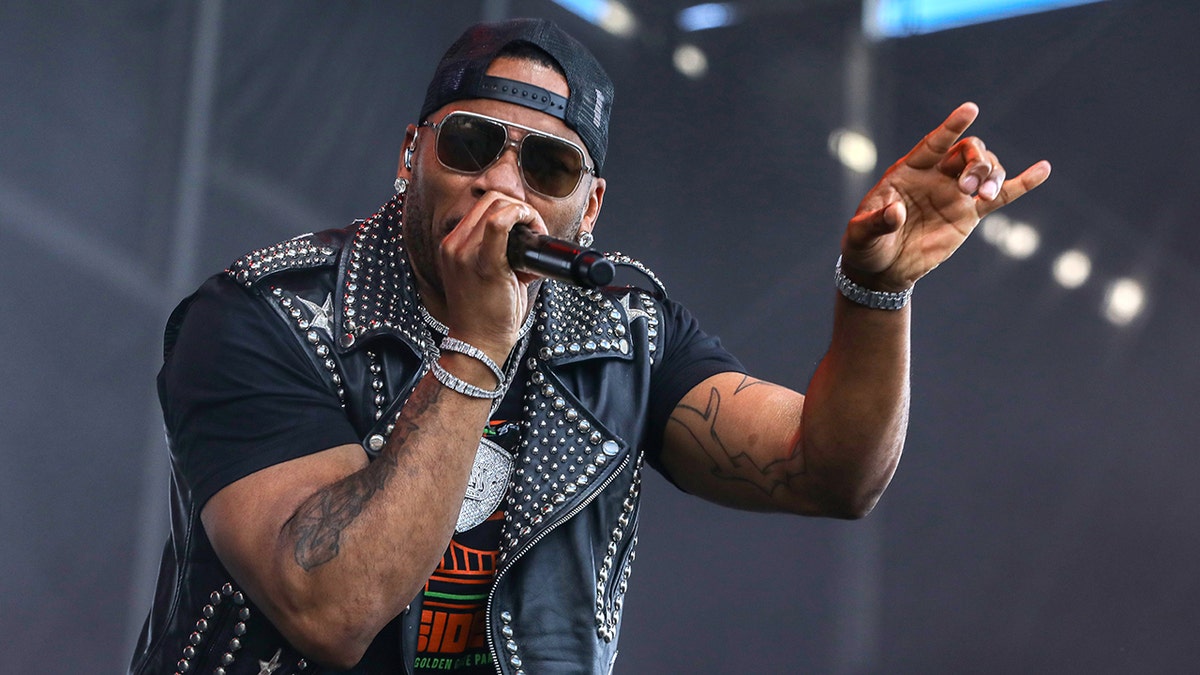 Nelly, wearing a studded leather jacket, points to the audience as she performs on stage 