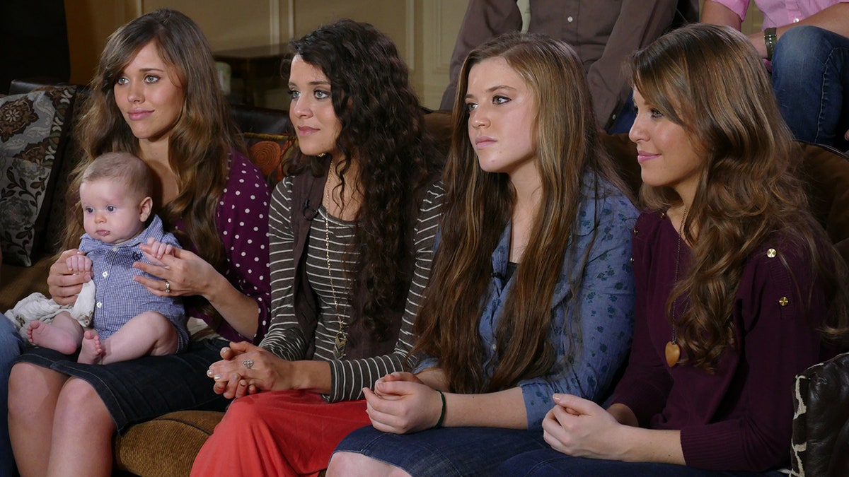 Jinger Duggar sitting down with her sisters as one holds a baby.