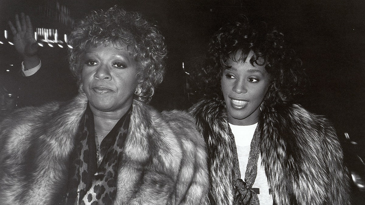 A black and white photo of Cissy Houston wearing a fur coat looking serious next to Whitney Houston.
