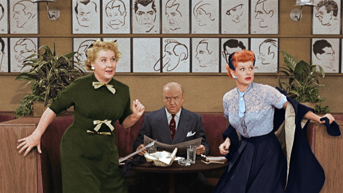 William Frawley sitting at a table in between a shock Vivian Vance and Lucille Ball