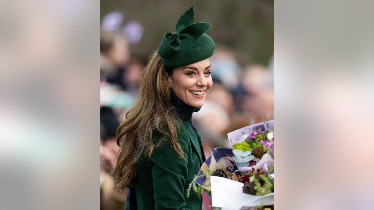 Kate Middleton sonriente con un abrigo verde y un sombrero a juego aceptando un ramo de flores.