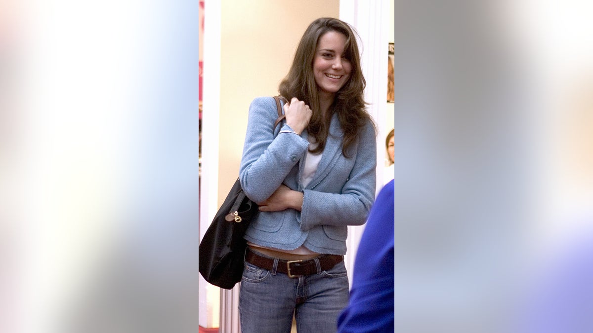 Kate Middleton wearing a light blue weater and jeans holding a black purse.