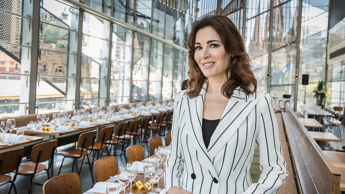 Nigella Lawson mengenakan blazer bergaris putih dan hitam di depan meja makan.