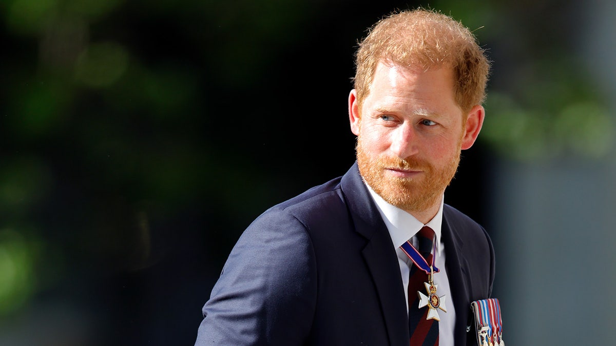 Prince Harry in a navy suit with media looking away