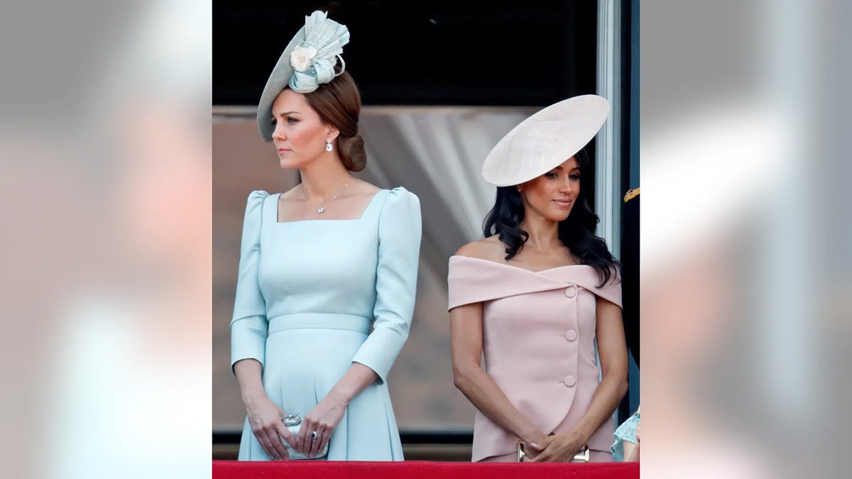 Kate Middleton wearing a pale blue dress turned away from Meghan Markle wearing a pink dress