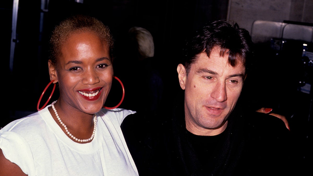 Robert De Niro wearing a black shirt holding onto Toukie Smith wearing a white shirt.