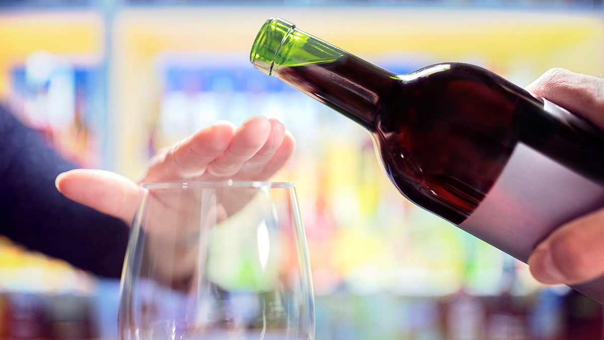 Person's hand rejects wine from being poured into their glass