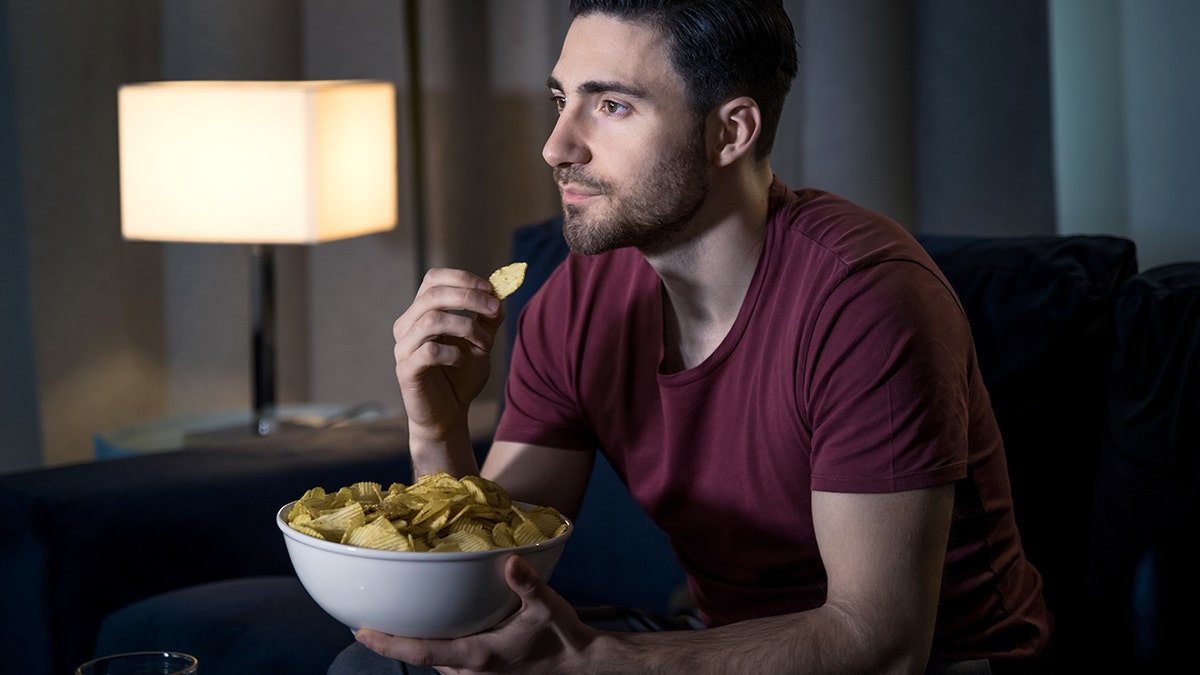 Jovem relaxando assistindo a filmes comendo batatas fritas.