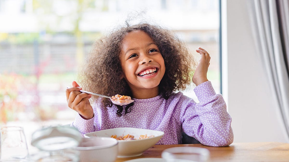 girl smiling while eating a bowl of cereal