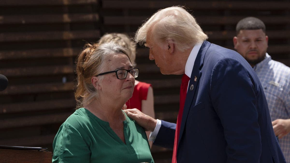 Patty Morin in green and Donald Trump in a navy blue suit speak at the border wall in Arizona