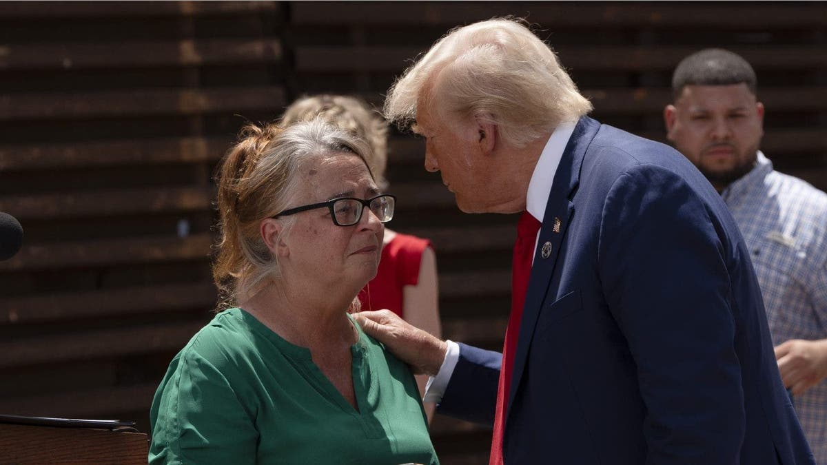 Patty Morin in green and Donald Trump in a navy blue suit speak at the border wall in Arizona
