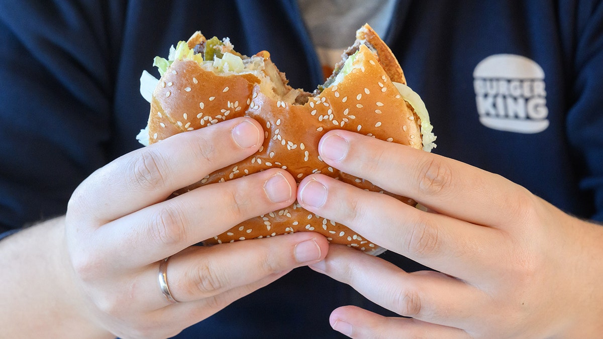 A person eats a large sandwich bearing the burger King's logo at the back