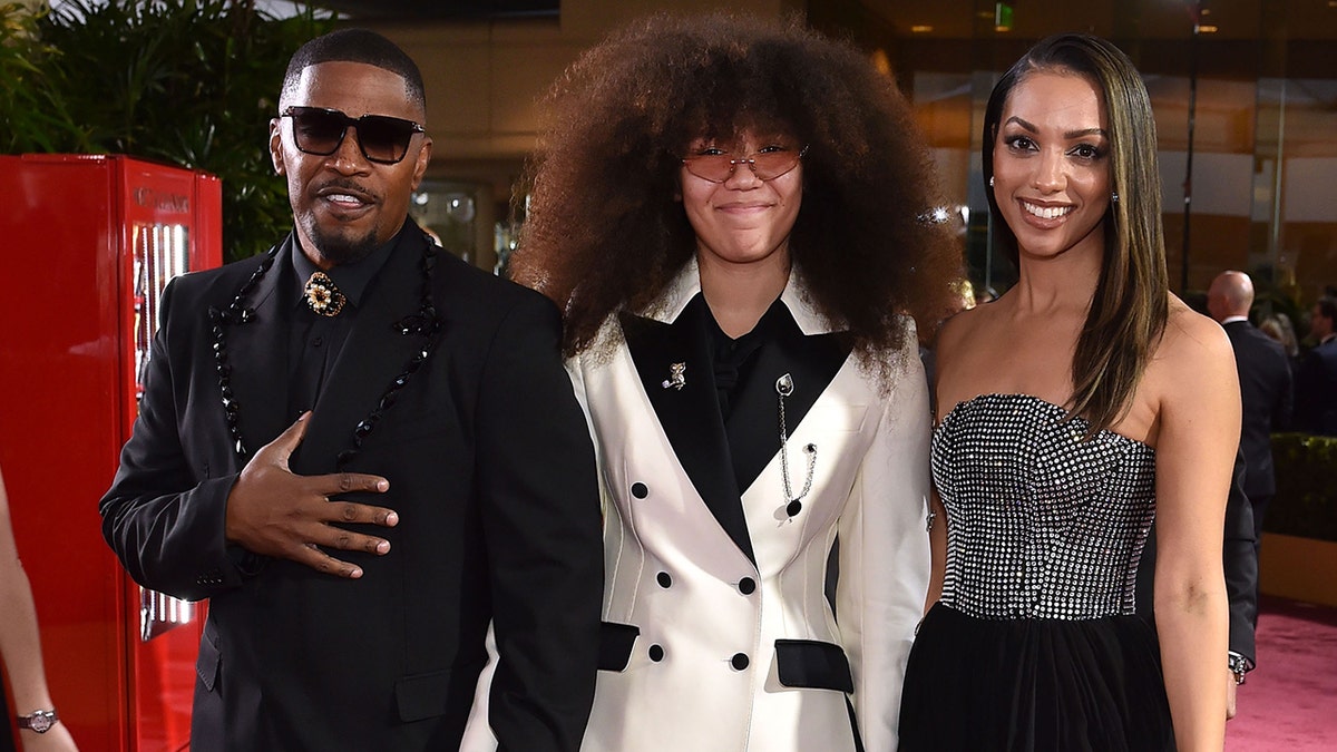 Jamie Foxx con traje negro posa con sus hijas Anelise y Corinne con americana blanca y vestido negro respectivamente en los Globos de Oro