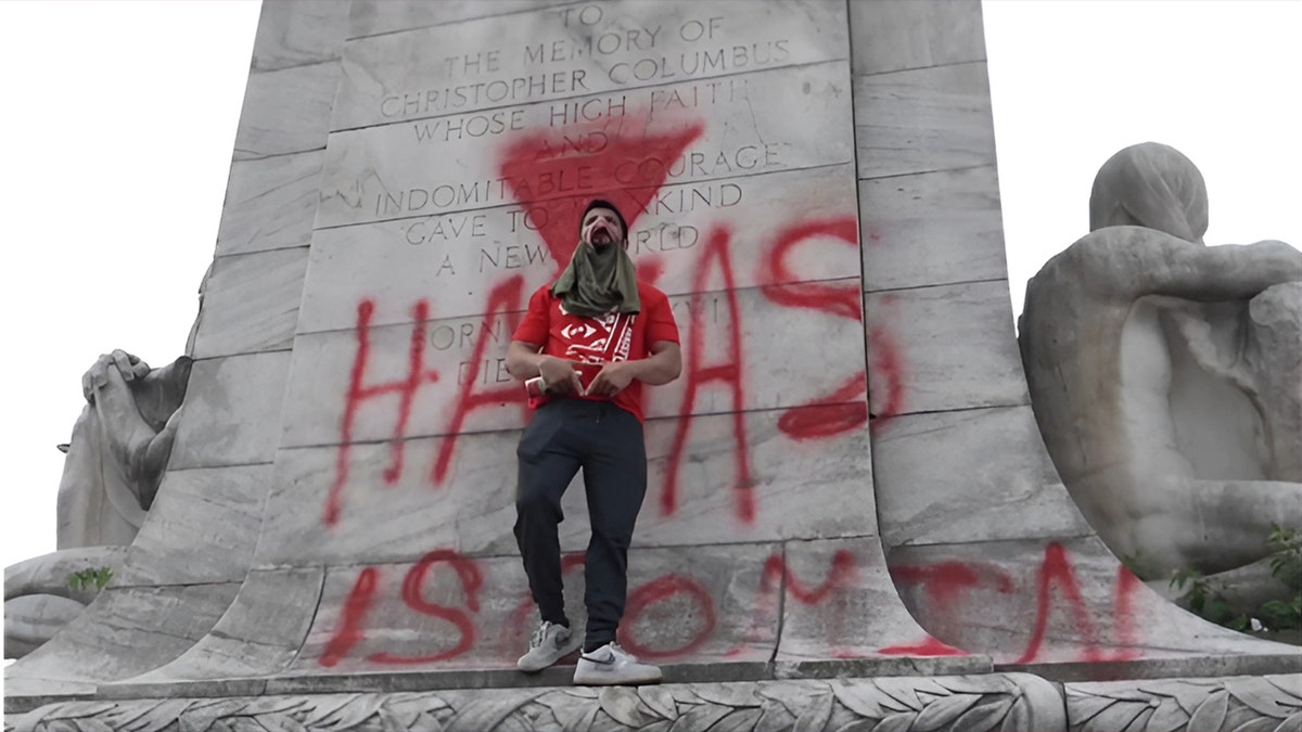 Man standing in front of Hamas graffiti