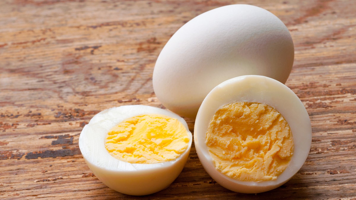 Hard-boiled eggs sit on a table, one cut in half and one whole.