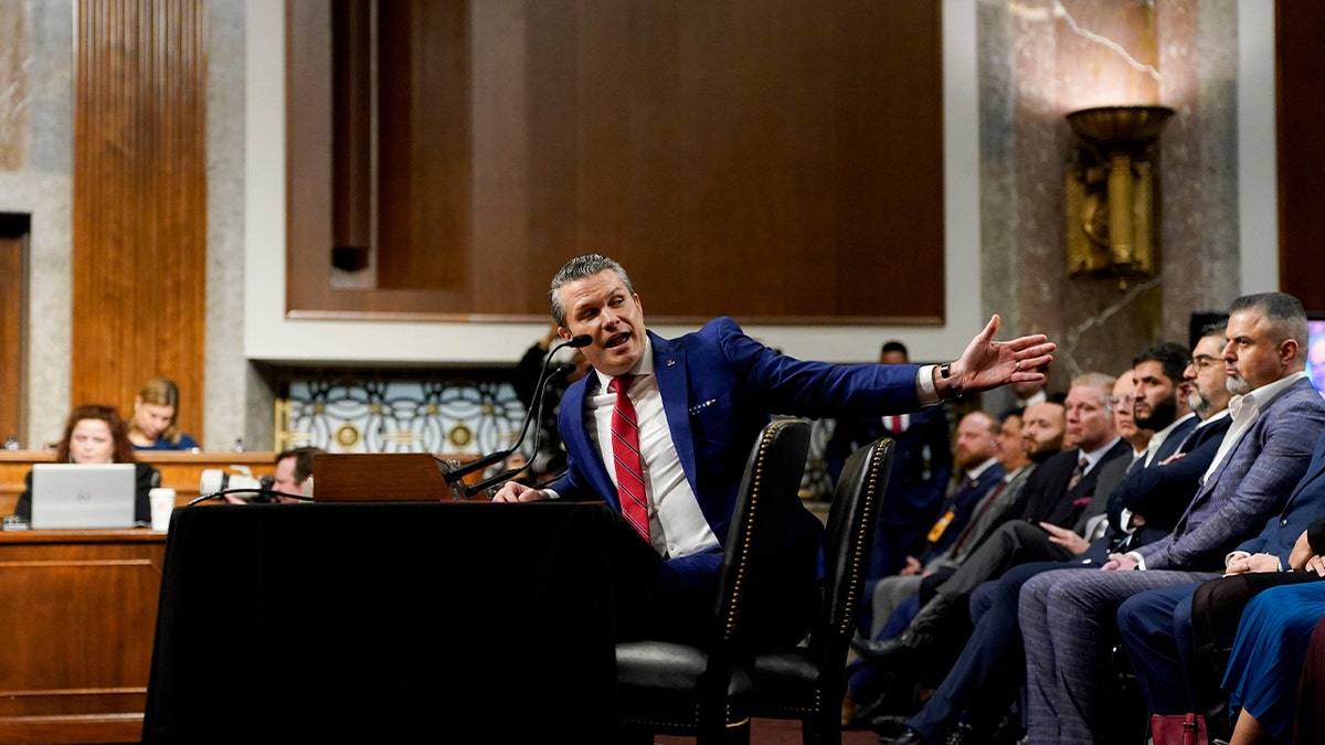 Hegseth at hearing table motioning to audience behind him