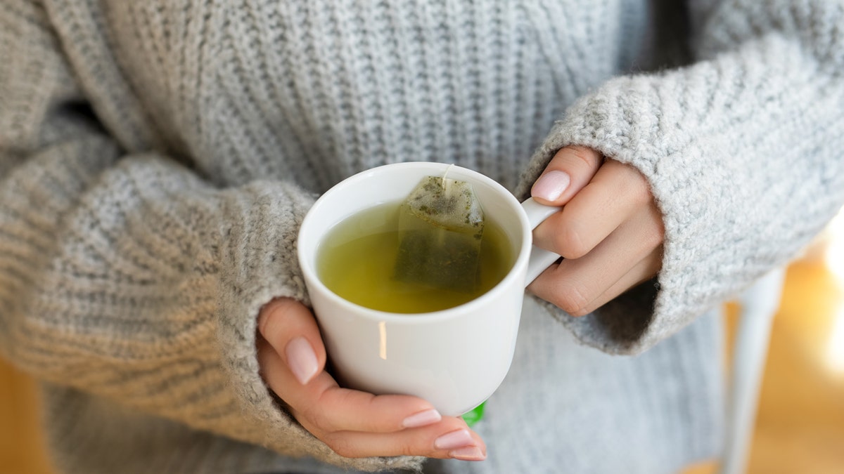 Hands hold a cup of green tea.