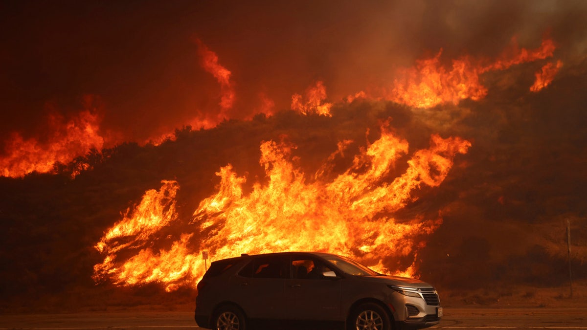 A vehicle rides past a hillside engulfed in flames caused by the Hughes Fire in Castaic, Calif., Wednesday.