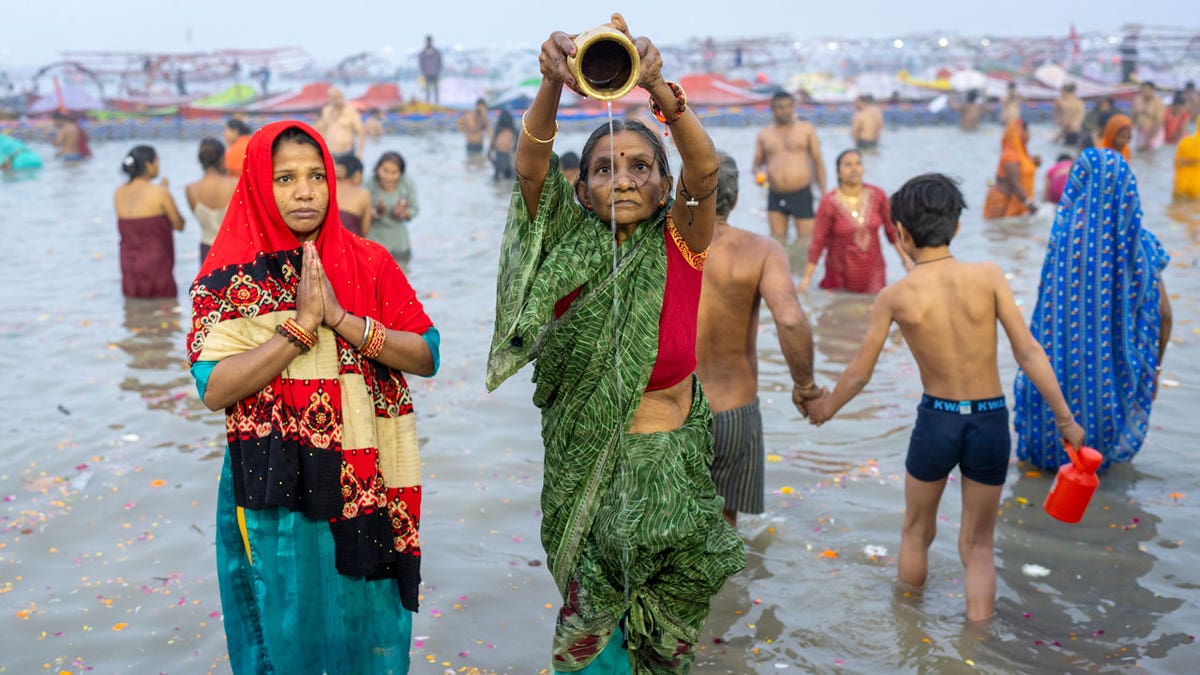 Hindu devotees pray before taking a dip in the water. One pours a pitcher into the river.