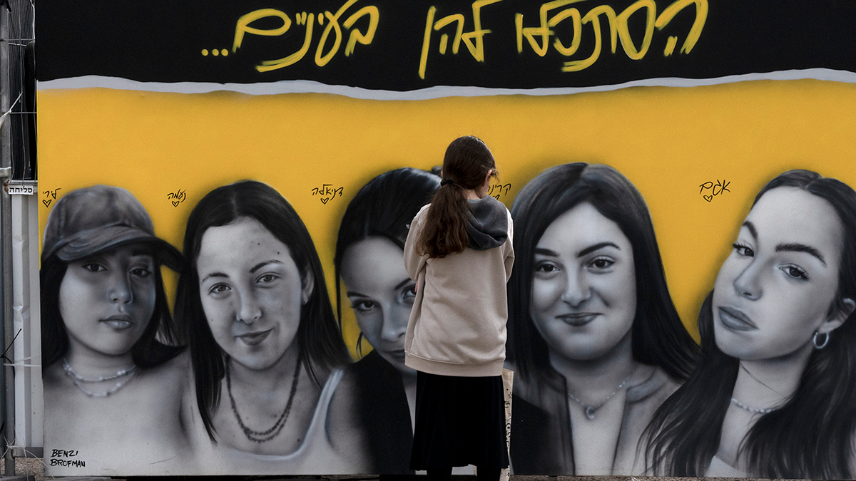 A girl pauses in front of a mural of Israeli female soldiers