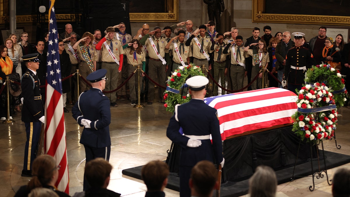 Pasukan Pramuka memberi hormat saat mereka memberikan penghormatan di depan peti mati yang dibungkus bendera pada Upacara Berbaring di Kenegaraan untuk mantan Presiden Jimmy Carter di Rotunda Capitol AS