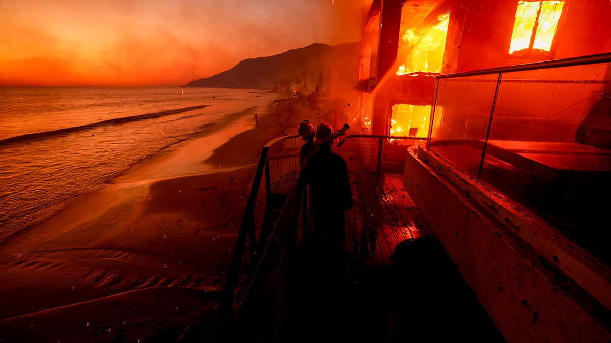 Firefighters work from a deck as the Palisades Fire burns a beachfront property