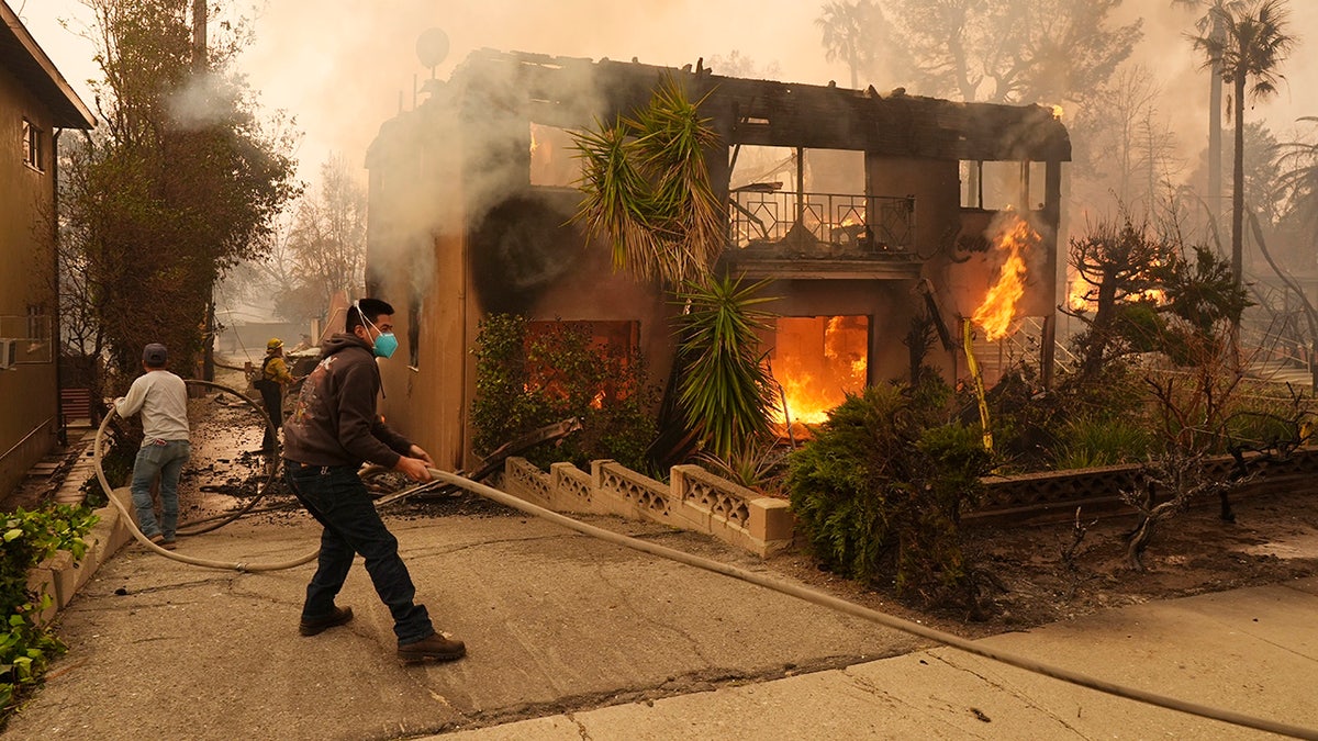 Pedestrians help a firefighter pull a hose as an apartment building burns