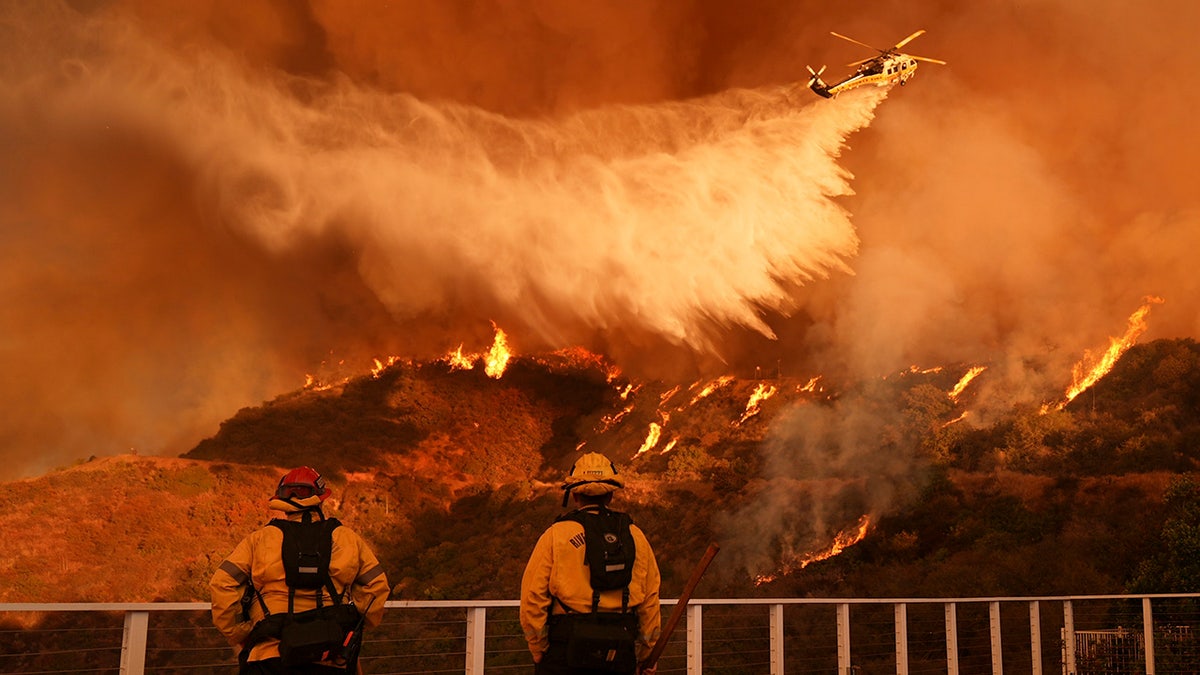 Firefighters watch as water falls on the Palisades Fire in Mandeville Canyon