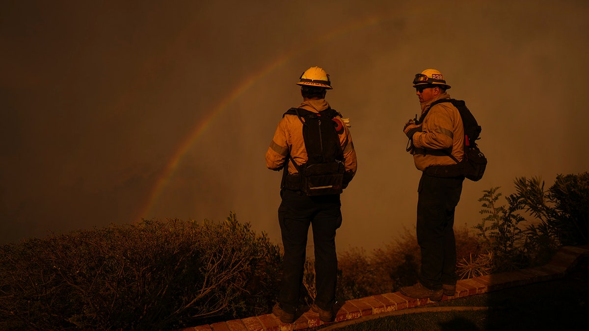 A rainbow rises over firefighters as they monitor the Palisades Fire