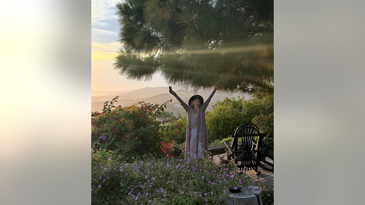 Ricki Lake raises her arms on her Malibu property as the sun sets in the background