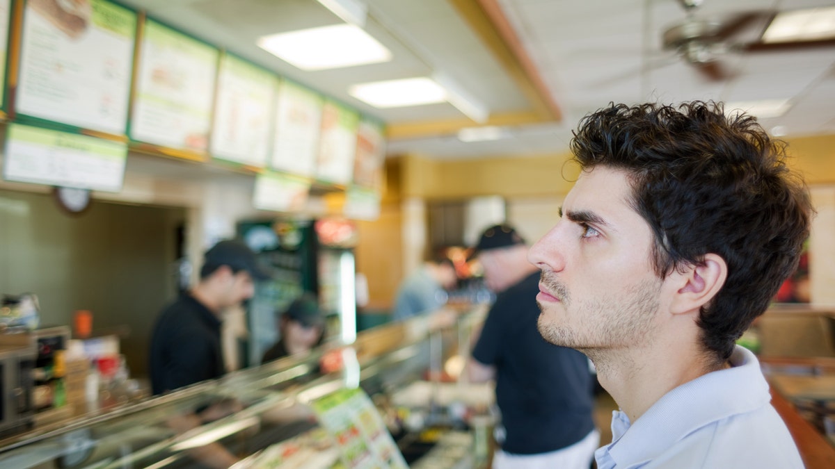 A man is looking at a menu above the counter and deciding what to order.