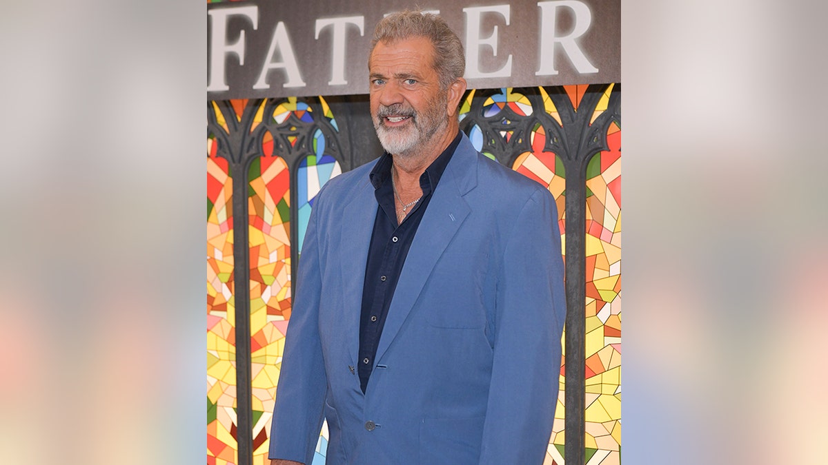 Mel Gibson smiles with a blue suit and a black carpet shirt