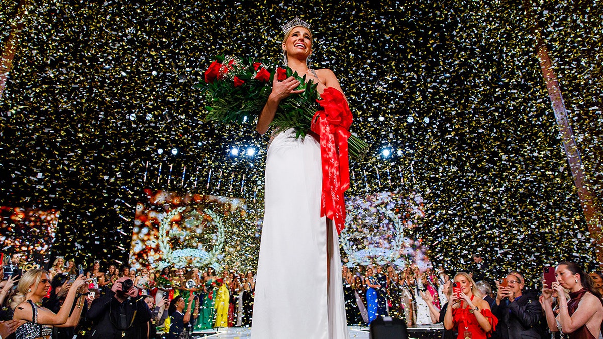 Miss America 2025 Abbie Stockward wearing a white gown and holding a bouquet of red roses.