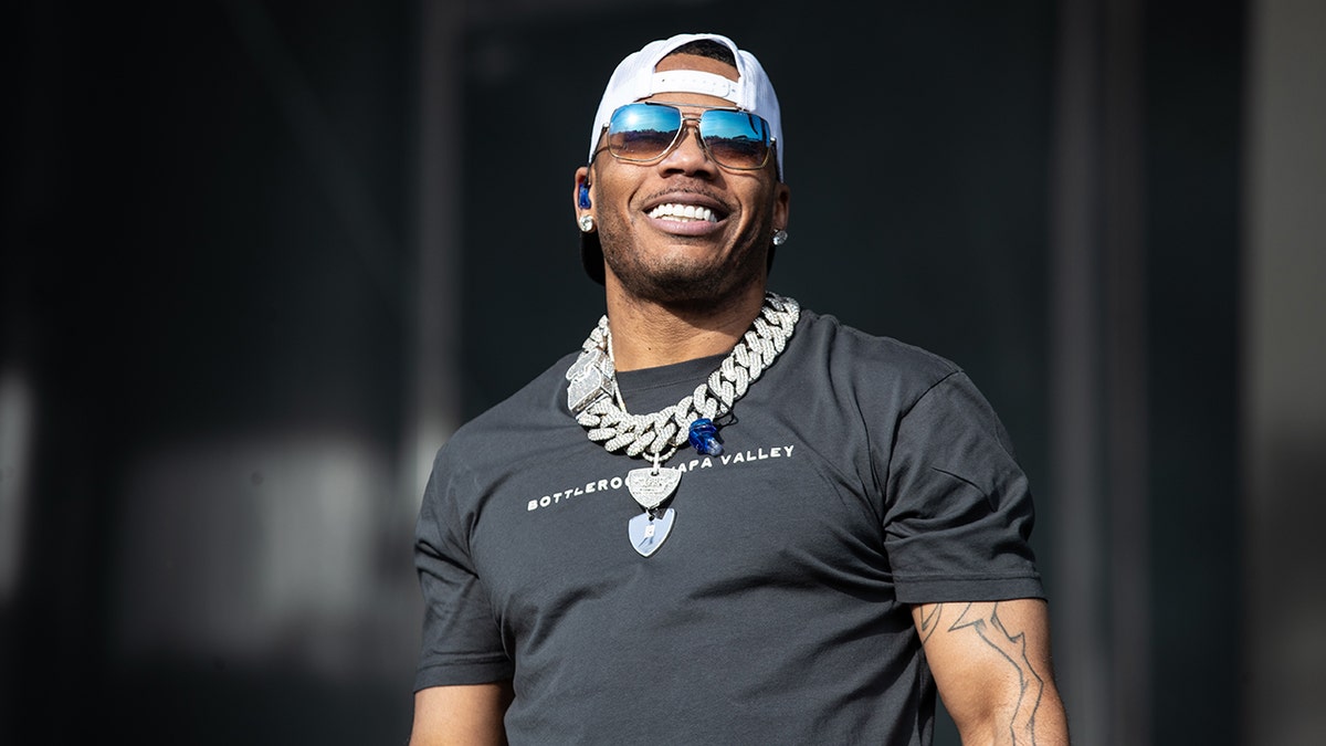 Nelly looks up on stage wearing a black t-shirt, a huge silver chain, backwards hat and blue-tinted sunglasses