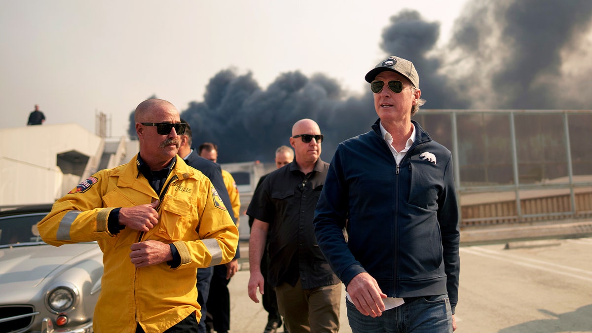 California Gov. Gavin Newsom, right, walks through the Pacific Palisades downtown business district as the Palisades Fire continues to burn on Jan. 8, 2025, in Los Angeles.