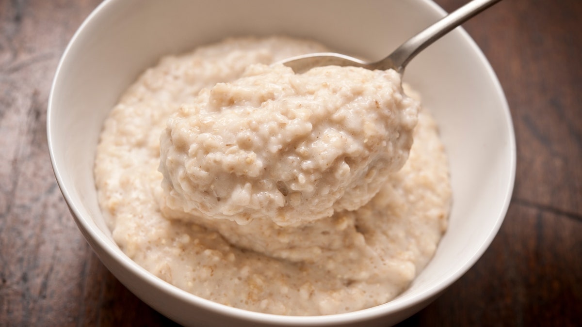 A spoonful of oatmeal comes out of a white bowl.