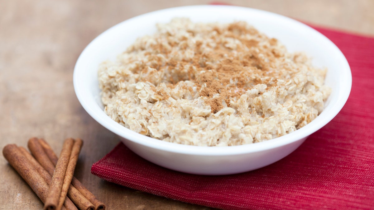 A bowl of oatmeal sits next to cinnamon sticks.