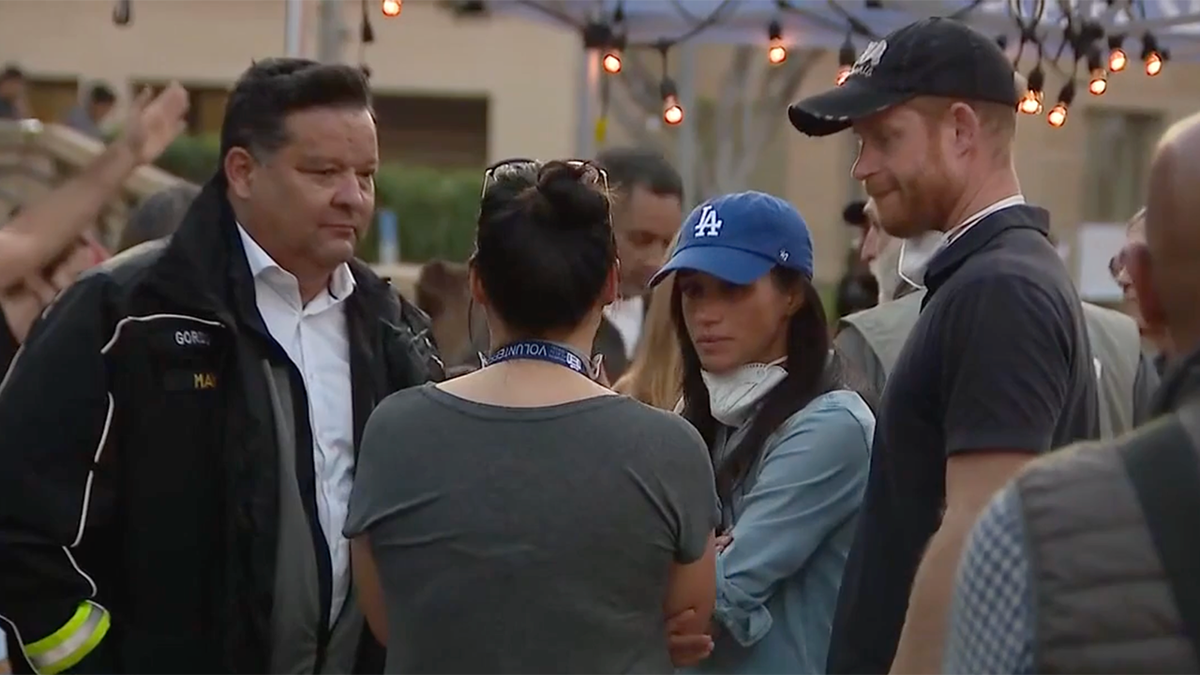 Victor Robo in a black jacket talks to a woman with her back to Meghan Markle in a green Dodgers hat and Prince Harry in Pasadena.