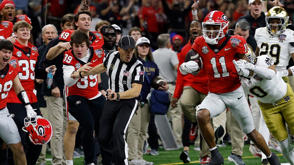 Georgia Bulldogs wide receiver Arian Smith, No. 11, runs with the ball after catching it while Irish safety Xavier Watts, No. 0, tries to tackle as sideline judge J.B. Garza collides with Bulldogs linebacker Parker Jones, No. 39, on the bench during Second quarter at Caesars Superdome on January 2, 2025.